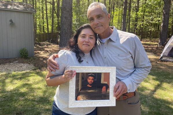 Patricia Ragan and her father, Rodrigo Arreola, hold a photo of her brother, Hector Arreola, outside of Rodrigo Arreola's home on April 11, 2023, in Columbus, Ga. The cause of Hector Arreola's death was changed from an accident to homicide caused by "sudden cardiac death following struggle with law enforcement including prone position restraint complicating acute methamphetamine toxicity.'' In 2021, his family was awarded $500,000 in a settlement with the city of Columbus. (Eve Sampson/Howard Center for Investigative Journalism via AP)