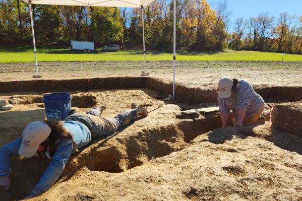 In this photo provided by John Crawmer, Jane C. Skinner and Samantha Muscella excavate post holes at the bottom of a stockade trench, Thursday, Oct. 27, 2022, in York, Pa. Researchers say they have solved a decades-old riddle by finding remnants of the stockade and therefore the site of a prison camp in York, that housed British soldiers for nearly two years during the American Revolutionary War. (John Crawmer via AP)