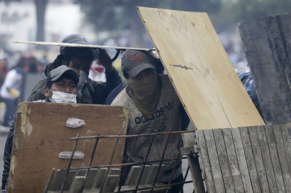 Anti-government demonstrators take cover behind a barricade during clashes with police in Quito, Ecuador, Saturday, Oct. 12, 2019. Protests, which began when President Lenin Moreno's decision to cut subsidies led to a sharp increase in fuel prices, have persisted for days. (AP Photo/Fernando Vergara)