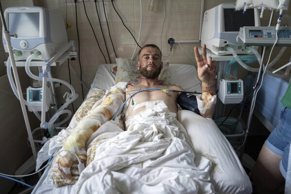 Kaiman, a Ukrainian serviceman, shows a Victory sign at the ICU of Mechnikov Hospital in Dnipro, Ukraine, Saturday, July 15, 2023. A surge of wounded soldiers has coincided with the major counteroffensive Ukraine launched last month to try to recapture its land from Russian forces. Surgeons at Mechnikov Hospital, one of the country's biggest, are busier now than perhaps at any other time since Russia began its invasion 17 months ago. (AP Photo/Evgeniy Maloletka)