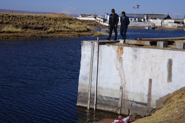 A military officer and an engineer stand near a water gauge that measures the water level of Lake Titicaca in the port of Guaqui, Bolivia, Thursday, July 27, 2023. The lake’s low water level is having a direct impact on the local flora and fauna and is affecting local communities that rely on the natural border between Peru and Bolivia for their livelihood. (AP Photo/Juan Karita)