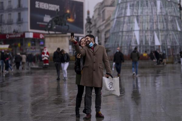 A couple take a selfie at Sol square in downtown Madrid, Spain, Friday, Dec. 24, 2021. The Spanish government has ordered mandatory mask-wearing outdoors, with few exceptions, starting from Friday. (AP Photo/Manu Fernandez)