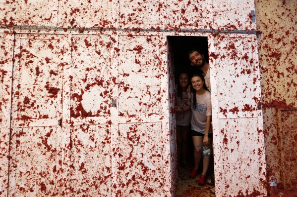 People are photographed inside a house during the annual tomato fight fiesta called "Tomatina" in the village of Bunol near Valencia, Spain, Wednesday, Aug. 30, 2023. Thousands gather in this eastern Spanish town for the annual street tomato battle that leaves the streets and participants drenched in red pulp from 120,000 kilos of tomatoes. (AP Photo/Alberto Saiz)