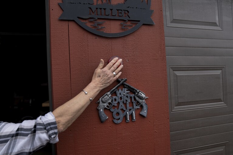 Kathy Miller, touches a light on her garage in Elmore, Vt., Monday, March 4, 2024, in remembrance of her late husband, Warren, above a sign he put up before passing away. In 2020, Warren died. He loved collecting things — advertising signs, beer-tap handles, snowboards. At home, Miller looks through some of his collections and talks about selling stuff. Her sense of loss is profound. Her best friend, the man she worked alongside every day, is gone. (AP Photo/David Goldman)