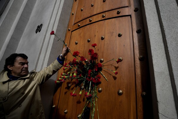 The relative of a person who was executed during Chile's dictatorship places a flower on the east side door of La Moneda presidential palace, through which the body of President Salvador Allende was carried by soldiers and firefighters 50 years ago after the military coup that toppled his government in Santiago, Chile, Monday, Sept. 11, 2023. (AP Photo/Esteban Felix)