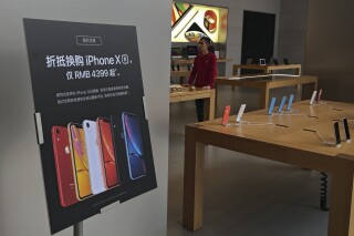 FILE - A trade-in for iPhone XR promotion board is displayed as an Apple employee waits for customers at its retail store in Beijing, Thursday, Jan. 3, 2019. Apple has agreed to pay $490 million to settle a class-action lawsuit alleging CEO Tim Cook misled investors about a steep downturn in the iPhone's sales in China that culminated in a jarring revision to the company's revenue forecast. The preliminary settlement was filed Friday, March 15, 2024, in Oakland, Calif., federal court. (AP Photo/Andy Wong, File)