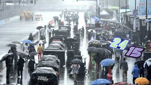 People walk along pit row in the rain before a NASCAR Cup Series auto race at the Grant Park 220 Sunday, July 2, 2023, in Chicago. (AP Photo/Morry Gash)