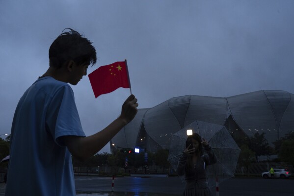 A person holding a Chinese flag poses for photographs outside the Hangzhou Olympic Sports Center Stadium ahead of the 19th Asian Games in Hangzhou, China, Friday, Sept. 21, 2023. (AP Photo/Louise Delmotte)