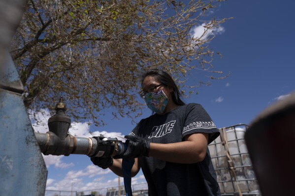 FILE - Raynelle Hoskie attaches a hose to a water pump to fill tanks in her truck outside a tribal office on the Navajo reservation, April 20, 2020, in Tuba City, Ariz. The Navajo Nation, a Native American tribe with one of the largest outstanding claims to water in the Colorado River basin, is closing in on a settlement with more than a dozen parties, putting it on a path to piping water to tens of thousands of tribal members in Arizona who still live without it. Negotiating terms outlined Wednesday, Feb. 28, 2024, include water rights not only for the Navajo Nation but the neighboring Hopi and San Juan Southern Paiute tribes in the northeastern corner of the state. (APPhoto/Carolyn Kaster, File)