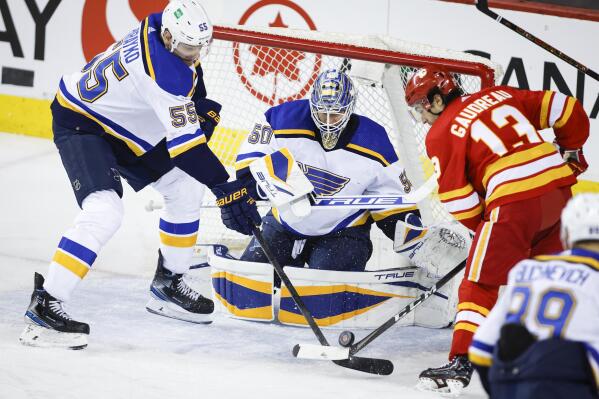 St. Louis Blues' Colton Parayko, left, and Calgary Flames' Johnny Gaudreau, right, battle for the puck as Blues goalie Jordan Binnington looks on during second-period NHL hockey game action in Calgary, Alberta, Monday, Jan. 24, 2022. (Jeff McIntosh/The Canadian Press via AP)