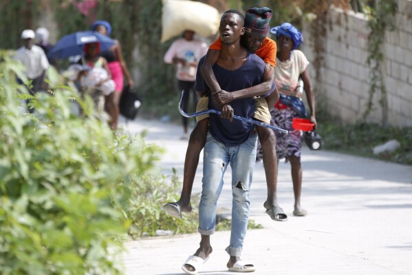 A resident carries an elderly man on his back as they flee their home to avoid clashes between armed gangs in the Pernier district of Petion-Ville, Haiti, Wednesday, Jan. 31, 2024. (AP Photo/Odelyn Joseph)