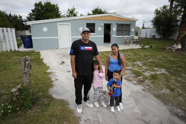 Alexis Llanos, left, his partner Diomaris Barboza, and their children Alexa, 7, and Alexis, 3, pose for a picture outside the home they moved into in October 2023, five years after fleeing Venezuela to Colombia to escape death threats and political persecution, in Lehigh Acres, Fla., Dec. 27, 2023. The family is among the first migrants allowed into the U.S. under the Biden administration's new "safe mobility offices," intended to streamline the U.S. refugee process so migrants don't give up and pay smugglers to make the journey north. (AP Photo/Rebecca Blackwell)