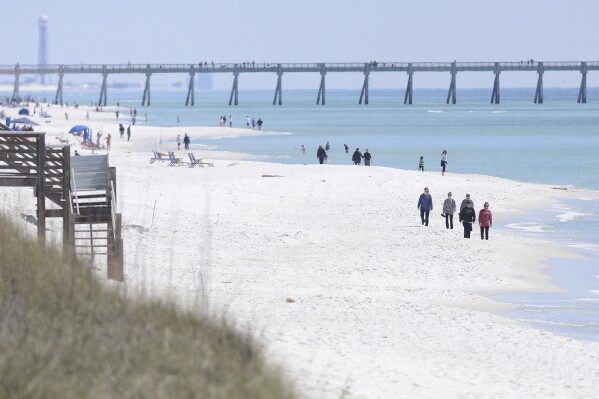 FILE - People walk along the shoreline in Navarre Beach, Fla., on Wednesday March 27, 2013. Authorities are warning of shark dangers this weekend along Florida’s Gulf Coast, where three people were hurt in two separate shark attacks Friday, June 7, 2024. (Nick Tomecek/Northwest Florida Daily News via AP)