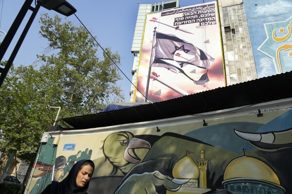 A woman walks past an anti-Israeli banner on a building at the Felestin (Palestine) Square in downtown Tehran, Iran, Sunday, April 14, 2024. Israel on Sunday hailed its air defenses in the face of an unprecedented attack by Iran, saying the systems thwarted 99% of the more than 300 drones and missiles launched toward its territory. The sign in Hebrew reads: 