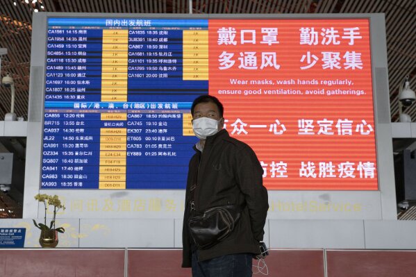 In this Thursday, March 12, 2020, photo, a man wearing a mask stands near a display board at the Capital International Airport terminal 3 in Beijing. As the number of new cases dwindles in China and multiplies abroad, the country once feared as the source of the COVID-19 outbreak is now worried about importing cases from abroad. China hasn't imposed any travel bans, but Beijing said this week that all people arriving from overseas would have to self-quarantine for 14 days. (AP Photo/Ng Han Guan)
