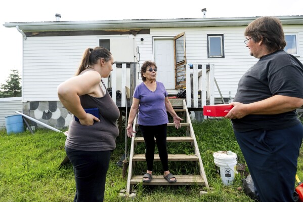 Carrol Johnston, center, who lost her home during a May wildfire, speaks with her son and daughter-in-law in the East Prairie Metis Settlement, Alberta, on Tuesday, July 4, 2023. Johnston, who has been living in a nearby town, is awaiting a modular home so she can return to the land. (AP Photo/Noah Berger)