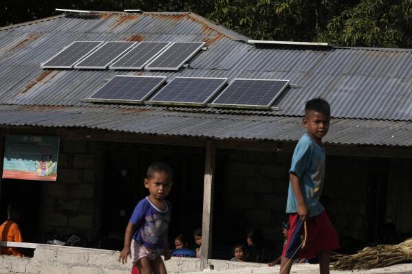 Children play near solar panels on the roof of house in Walatungga village on Sumba Island, Indonesia, Tuesday, March 21, 2023. Around the world, hundreds of millions of people live in communities without regular access to power, and off-grid solar systems like these are bringing limited access to electricity to places like these years before power grids reach them. (AP Photo/Dita Alangkara)