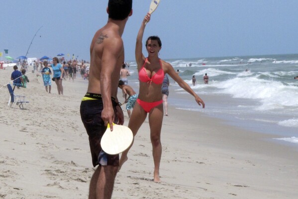 Beachgoers play paddle ball on the beach in Ship Bottom, N.J. on June 30, 2014. On Aug. 4, 2023, a German wind power company and a New York utility applied for permission to build a wind farm 37 miles off the coast of Long Beach Island, far enough out to sea that it could not be seen from the beach. (AP Photo/Wayne Parry)