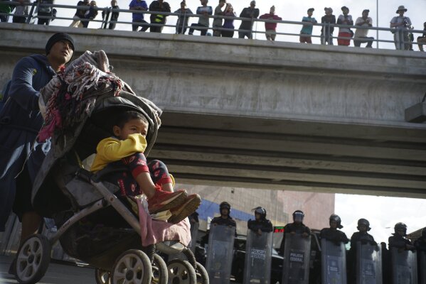 
              A migrant man pushes a child in a baby stroller past a cordon of riot police as he joins a small group of migrants trying to cross the border together at the Chaparral border crossing in Tijuana, Mexico, Thursday, Nov. 22, 2018. A small group of Central American migrants marched peacefully to a border crossing in Tijuana Thursday to demand better conditions and push to enter the U.S. (AP Photo/Ramon Espinosa)
            