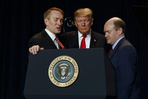 FILE - In this Feb. 7, 2019, file photo, Rep. James Lankford, left, R-Okla.; President Donald Trump, center; and Sen. Chris Coons, D-Del., pray during the National Prayer Breakfast in Washington. When Coons speaks to the Democratic National Convention on Thursday, Aug. 20, 2020, before Joe Biden’s speech accepting the party’s presidential nomination, his remarks will focus on faith — attesting in highly personal fashion to his longtime friend’s belief in God. (AP Photo/ Evan Vucci, File)