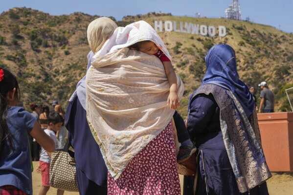 Tourists protect a sleeping child from the sun as they visit the Hollywood sign landmark in Los Angeles, Wednesday, July 12, 2023. (AP Photo/Damian Dovarganes)