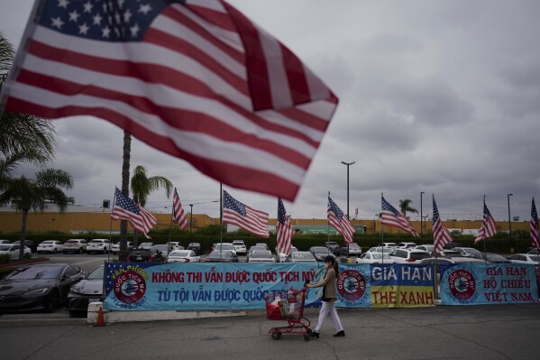 A woman pushes a shopping cart past rows of American flags and banners advertising U.S. citizenship and immigration services in the Little Saigon neighborhood of Garden Grove, Calif., Wednesday, April 23, 2025. (AP Photo/Jae C. Hong)