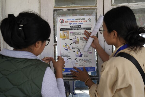 Polling officers Neichutuonuo Yhome, 27, left, and Neke W Konyak, 29, put up election posters at their assigned polling station on the eve of polls in Chedema village, in the northeastern Indian state of Nagaland, Thursday, April 18, 2024. (AP Photo/Yirmiyan Arthur)