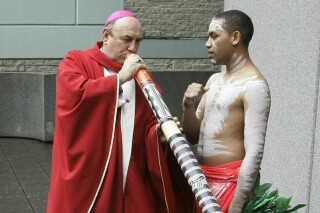 FILE - Bishop Christopher Saunders of Broome tries to play a digeridoo during a World Youth Day 2008 media event in Sydney, Australia, on April 17, 2008. The Vatican is considering the findings of a church investigation into “very serious and deeply distressing” child sexual abuse allegations against former Australian Bishop Saunders, a church leader said on Tuesday, Sept. 19, 2023. (AP Photo/Rob Griffith, File)