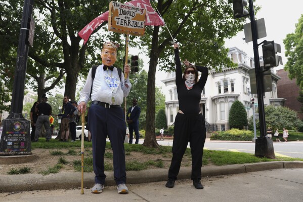 A demonstrator with a flag and another wearing a President Donald Trump mask carrying a sign participate in a protest taking place on the day of a military parade commemorating the Army's 250th anniversary, coinciding with Trump's 79th birthday, Saturday, June 14, 2025, in Washington. (AP Photo/Evan Vucci)