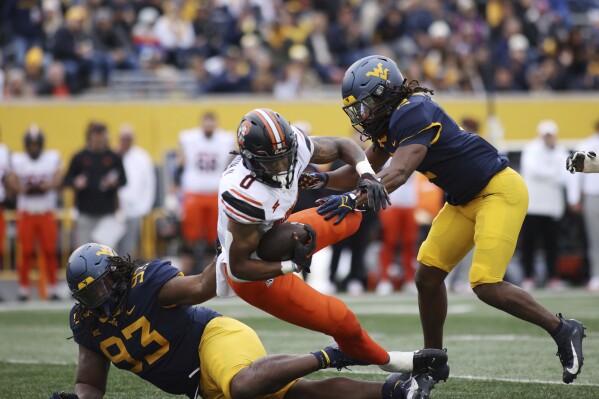 West Virginia's Mike Locker (93) and Aubrey Banks (2) tackle Oklahoma State's Ollie Gordon (0) during the first half of an NCAA college football game Saturday, Oct. 21, 2023, in Morgantown, W.Va. (AP Photo/Chris Jackson)