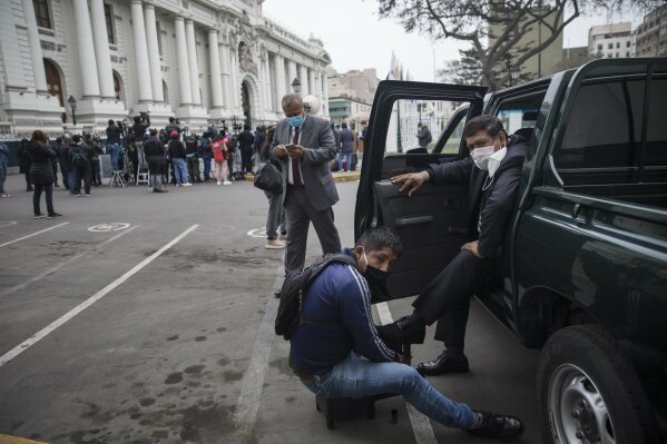 A shoe shiner works on a police officer's shoes during his break from providing security to Congress in Lima, Peru, Friday, Sept. 18, 2020. Peruvian President Martin Vizcarra’s job is on the line Friday as opposition lawmakers push through an impeachment hearing criticized as a hasty and poorly timed ouster attempt in one of the countries hardest hit by the coronavirus pandemic. (AP Photo/Rodrigo Abd)