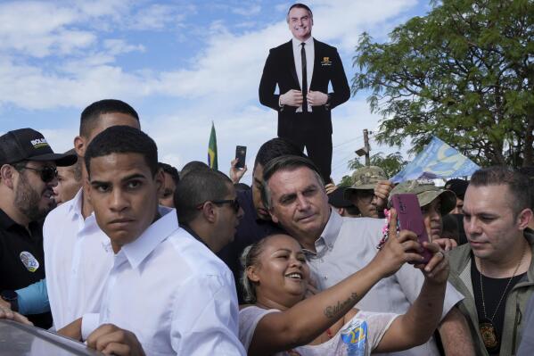 Brazil's President Jair Bolsonaro, center, takes a photo with a supporter as he campaigns for reelection at the rural workers' settlement Nova Jerusalem, or New Jerusalem, in Brasilia, Brazil, Monday, Oct. 24, 2022. Bolsonaro is running in the presidential runoff set for Oct. 30. (AP Photo/Eraldo Peres)