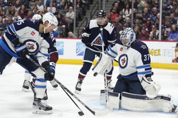 Winnipeg Jets defenseman Brenden Dillon, front left, blocks Colorado Avalanche right wing Mikko Rantanen, back left, as his shot on the net is stopped by Jets goaltender Connor Hellebuyck during the third period of an NHL hockey game Thursday, Dec. 7, 2023, in Denver. (APPhoto/David Zalubowski)