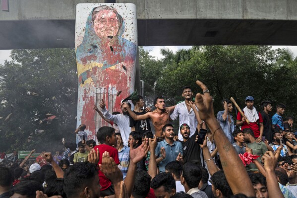 Protesters celebrate beside a defaced portrait of Prime Minister Sheikh Hasina after news of her resignation, in Dhaka, Bangladesh, Monday, Aug. 5, 2024. (AP Photo/Fatima Tuj Johora, File)