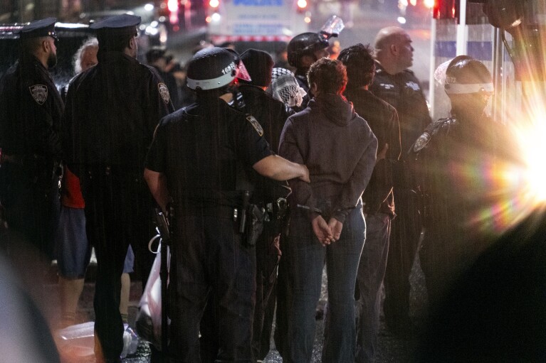 Podczas lekkiego deszczu funkcjonariusze policji Nowego Jorku zatrzymują ludzi w pobliżu kampusu Uniwersytetu Columbia w Nowym Jorku, wtorek, 30 kwietnia 2024 r., po oczyszczeniu z obozu namiotowego budynku przejętego przez protestujących.  (AP Photo/Craig Ruttle)