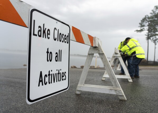Paul Lightfood and Travis Traylor, with Montgomery County Precinct 1, put up barricades and signs at the boat ramp entrance to Lake Conroe at FM 830, Wednesday, Jan. 24, 2024, in Conroe, Texas. The San Jacinto River Authority closed the lake to boating and other activities for safety reasons after the region was hit with its third day of widespread rainfall. (Jason Fochtman/Houston Chronicle via AP)