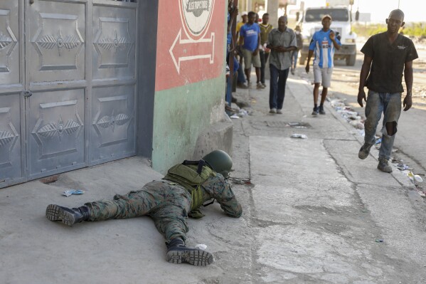 Pedestrians was past a soldier guarding the area of the international airport in Port-au-Prince, Haiti, Monday, March 4, 2024. (AP Photo/Odelyn Joseph)