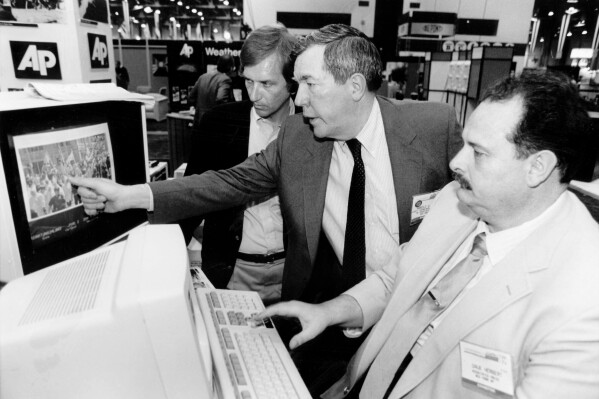 FILE - The Associated Press' assistant general manager for news photos Hal Buell, center, and Dave Herbert, right, the consultant who wrote the electronic darkroom software, explain PhotoStream at the American Newspaper Publishers Association technical convention in Las Vegas in June 1987. Buell, who led The Associated Press' photo operations from the darkroom era into the age of digital photography over a four-decade career with the news organization that included 12 Pulitzer Prizes and running some of the defining images of the Vietnam War, has died. Buell died Monday, Jan. 29, 2024, in Sunnyvale, Calif., where his daughter lived, after battling pneumonia. He was 92. (AP Photo)