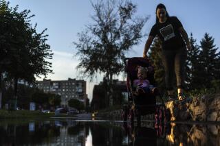 A mother pushes her child in a carriage through a puddle after a rainstorm in Pokrovsk, Donetsk region, eastern Ukraine, Thursday, Aug. 4, 2022. (AP Photo/David Goldman)