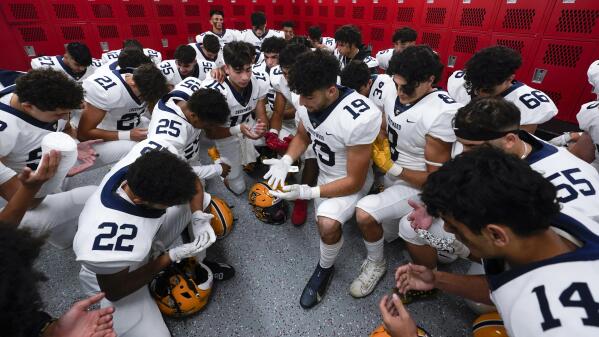 Crestwood High School football player Adam Berry (19) leads a muslim prayer before a game in Melvindale, Mich., Friday, Sept. 23, 2022. At Crestwood High School, where most of the football team is Muslim, the entire team gathers before practices and games to pray on one knee. (AP Photo/Paul Sancya)