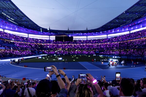 The crowd wears glowing wristbands as the lights are turned down inside the Stade de France for the start of the men's 100-meter final at the 2024 Summer Olympics, Sunday, Aug. 4, 2024, in Saint-Denis, France. (AP Photo/David Goldman)