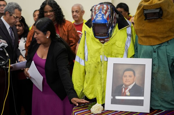 Maria del Carmen Castellón, the wife of Miguel Luna, a welder who died during the collapse of Baltimore's Francis Scott Key Bridge, places a rose near a portrait of her husband and his welding gear before speaking during a press conference, Tuesday, Sept. 17, 2024, in Baltimore. (AP Photo/Stephanie Scarbrough)