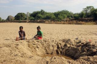 FILE - In this Nov. 11, 2020, file photo, children sit by a dug out water hole in a dry river bed in the remote village of Fenoaivo, Madagascar. Lola Castro, WFP’s regional director in southern Africa, told a news conference Friday, June 25, 2021, that she witnessed “a very dramatic and desperate situation” during her recent visit with WFP chief David Beasley to the Indian Ocean island nation of 26 million people.(AP Photo/Laetitia Bezain, File)