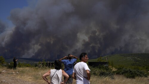 Residents watch as a wildfire burns on a hill in Pournari village near Athens, on Tuesday, July 18, 2023. In Greece, where a second heatwave is expected to hit Thursday, three large wildfires burned outside Athens for a second day. Thousands of people evacuated from coastal areas south of the capital returned to their homes Tuesday when a fire finally receded after they spent the night on beaches, hotels and public facilities. (AP Photo/Thanassis Stavrakis)