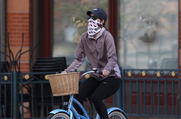 A bicyclist wears face protection against the new coronavirus while pedaling through Larimer Square early Saturday, April 25, 2020, in downtown Denver. (AP Photo/David Zalubowski)