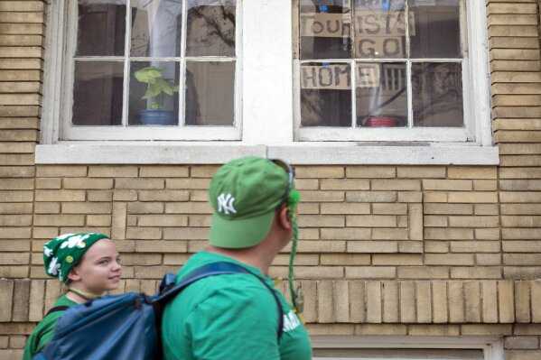 A family dressed in St. Patrick's Day attire walks past a window with a message for tourist, Tuesday, March, 17, 2020, in downtown Savannah, Ga. Due to concerns about coronavirus Savannah's mayor called off the city's 196-year-old St. Patrick's Day parade. (AP Photo/Stephen B. Morton)