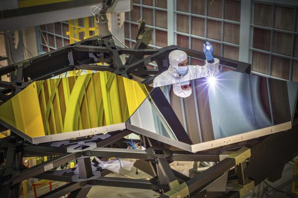 In this Sept. 29, 2014 photo made available by NASA, James Webb Space Telescope Optical Engineer Larkin Carey examines two test mirror segments on a prototype at the Goddard Space Flight Center's giant clean room in Greenbelt, Md. Webb will attempt to look back in time 13.7 billion years, a mere 100 million years after the universe-forming Big Bang as the original stars were forming. (Chris Gunn/NASA via AP)