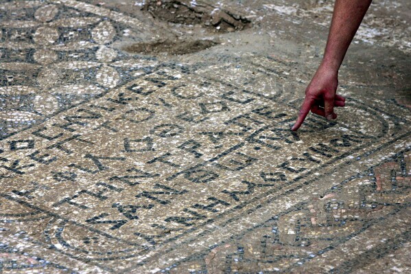 FILE - An Israeli archaeologist points at a nearly 1,800-year-old decorated floor from an early Christian prayer hall that Israeli archaeologists discovered on Sunday, Nov. 6, 2005, in the Megiddo prison. Israeli officials are considering uprooting the mosaic and loaning it to the controversial Museum of the Bible in Washington D.C., a proposal that has upset archaeologists and underscores the hardline government's close ties with evangelical Christians in the U.S. (AP Photo/Ariel Schalit, File)