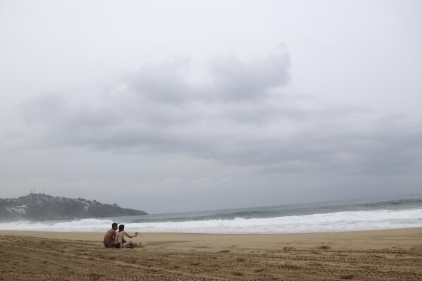 FILE - Tourists sit on the beach in Acapulco, Mexico, Tuesday, Oct. 24, 2023. Tourists have barely started trickling back into the Mexican resort of Acapulco, but the gangland killings on the beaches have already returned. At least three people were shot to death on the beach in Acapulco last weekend. (AP Photo/Bernardino Hernandez, File)