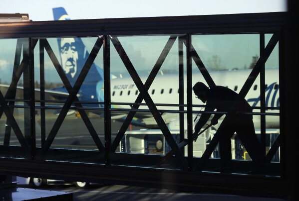 FILE - A worker cleans a jet bridge at Paine Field in Everett, Wash., before passengers board an Alaska Airlines flight on March 4, 2019. Seattle-based Alaska Airlines owns Horizon Air. An off-duty pilot riding in the extra seat in the cockpit of a Horizon Air passenger jet on Sunday, Oct. 22, 2023, tried to shut down the engines in mid-flight and had to be subdued by the crew, according to a pilot flying the plane. (AP Photo/Ted S. Warren, File)